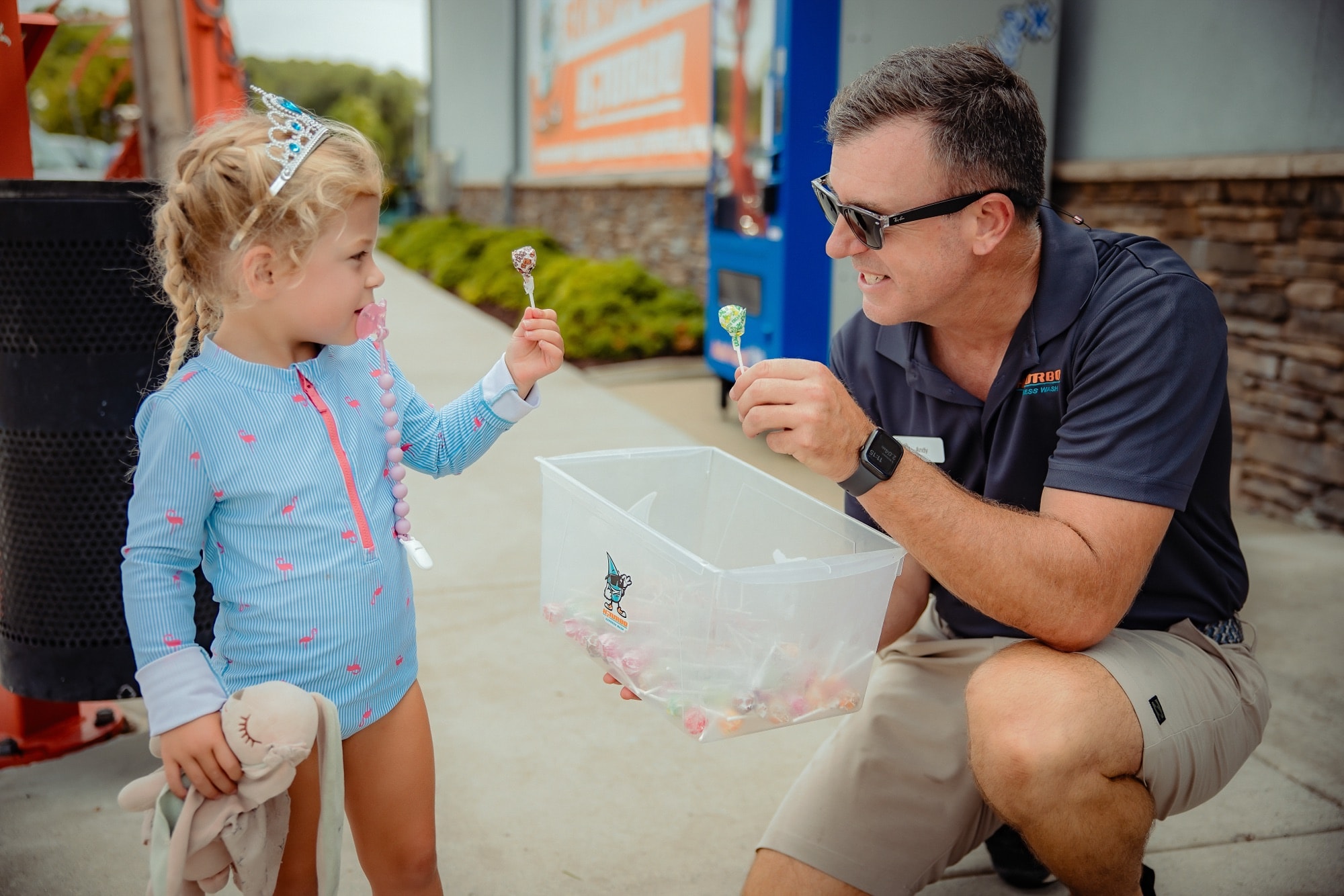 Andy handing a lollipop to a young customer in a tiara